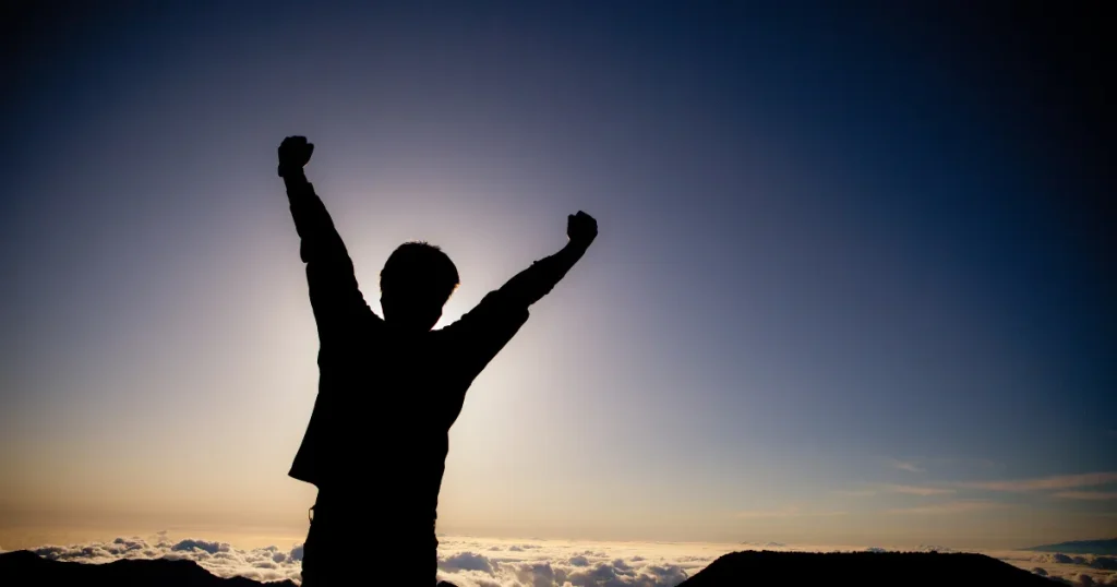 山頂で勝利のポーズをとる人のシルエット